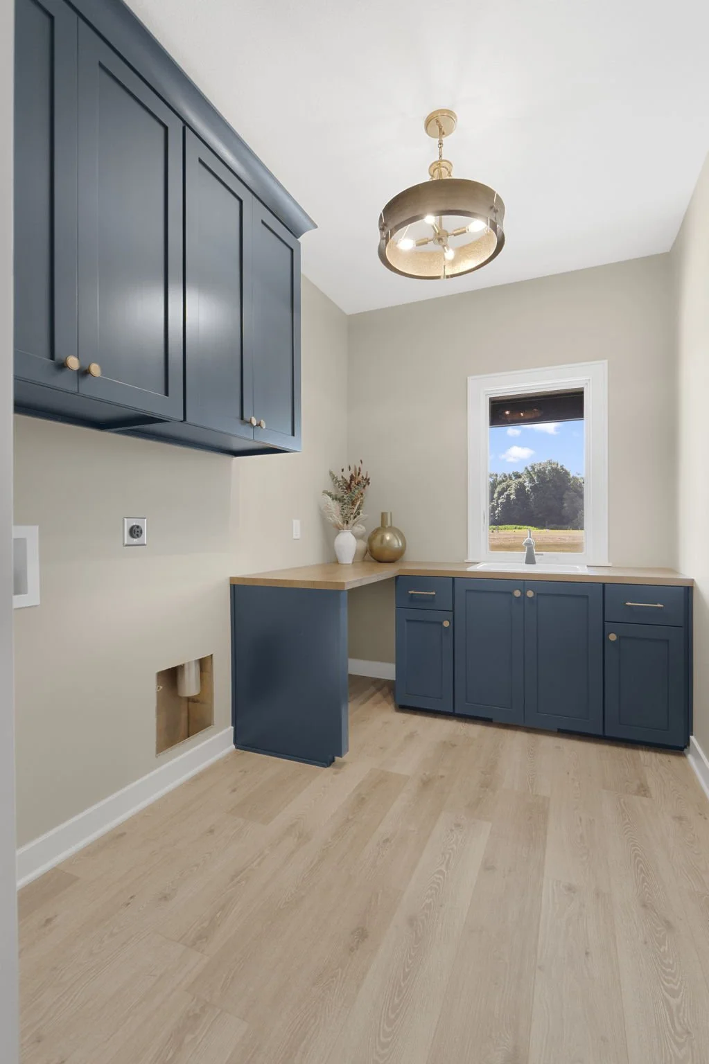 Kitchen with light wood flooring, beige walls, blue cabinets, a window looking outside, and decorative vases on the counter.