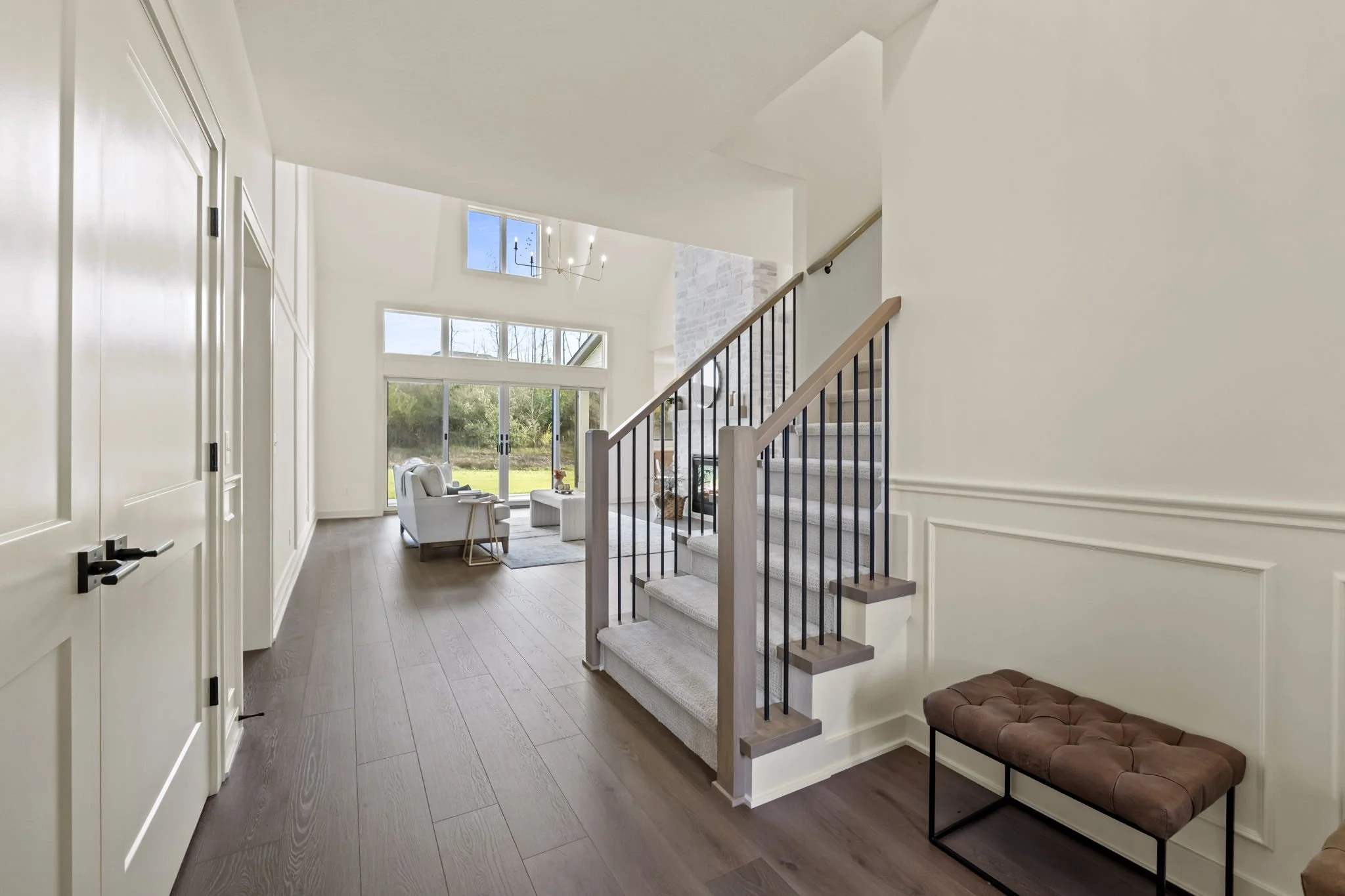 Interior view of a modern living space with stairs, a seating area with white sofas, a large window, and sliding glass doors leading outside.