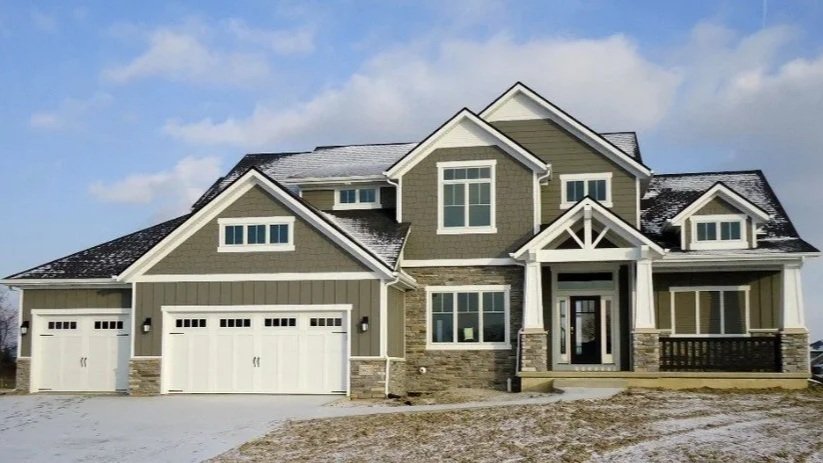 Modern two-story house with a garage, front porch, and stone accents, under a partly cloudy sky.