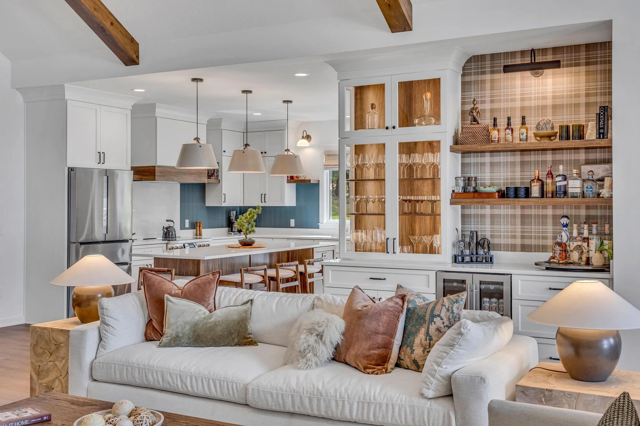 Open plan kitchen and living room with white cabinetry, blue backsplash, wooden accents, and a white sofa with decorative pillows.