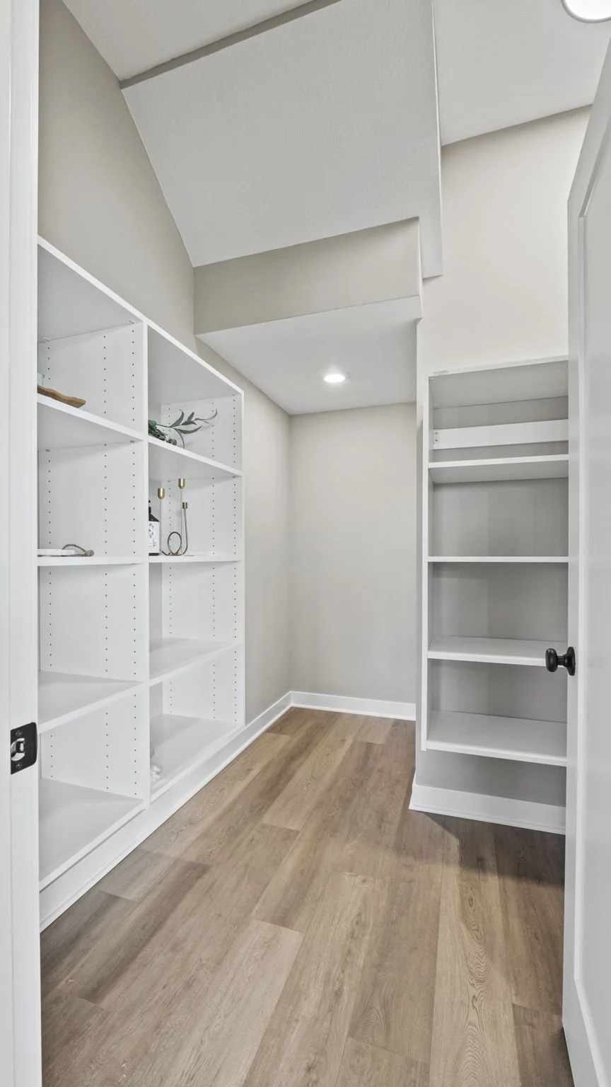 Empty walk-in closet with white shelves and wood flooring.