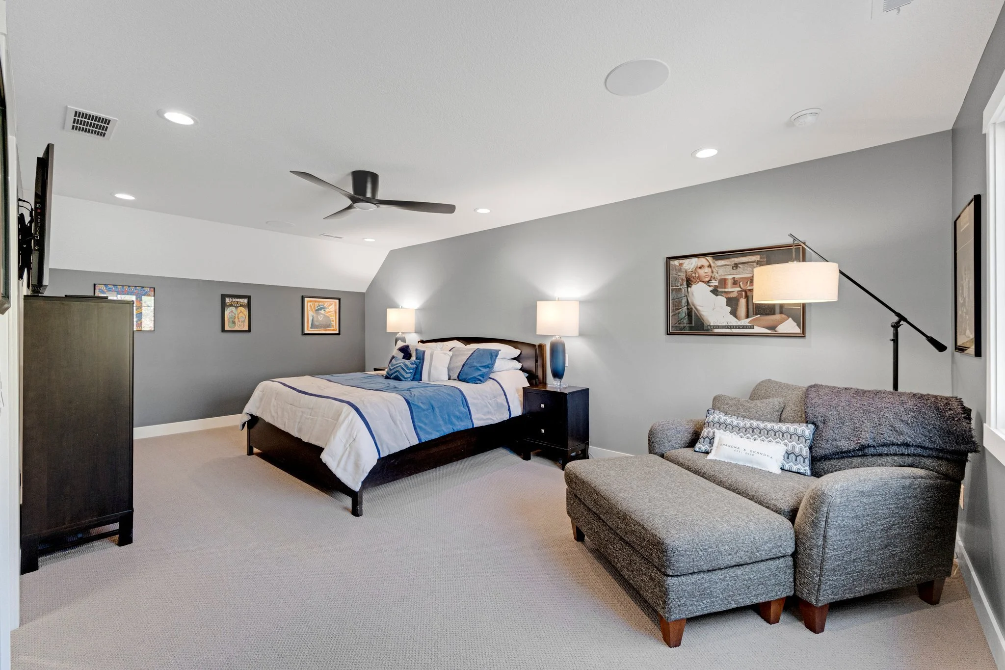 A modern bedroom featuring a bed with blue and white bedding, two nightstands with lamps, a gray sofa with pillows, and artwork on the walls.