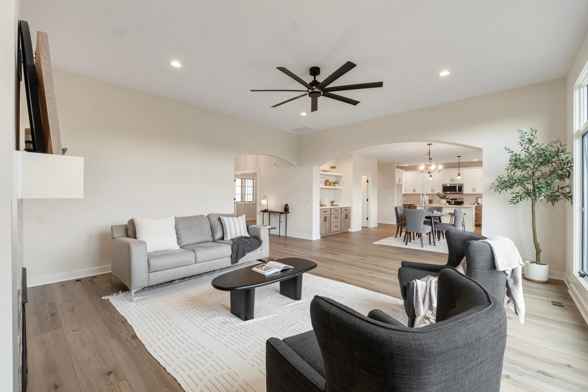 Living room with light-colored sofa, dark armchairs, coffee table, area rug, and open view to dining area and kitchen.