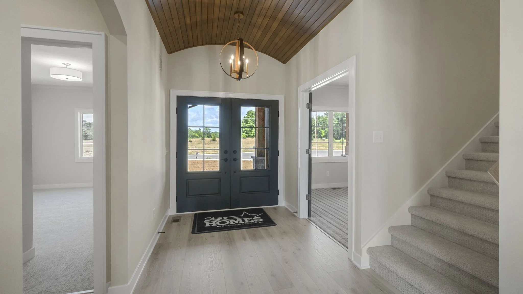 Entryway with dark blue front doors, wooden ceiling, modern chandelier, light-colored hardwood floor, and a welcome mat that says "Start at HOME".