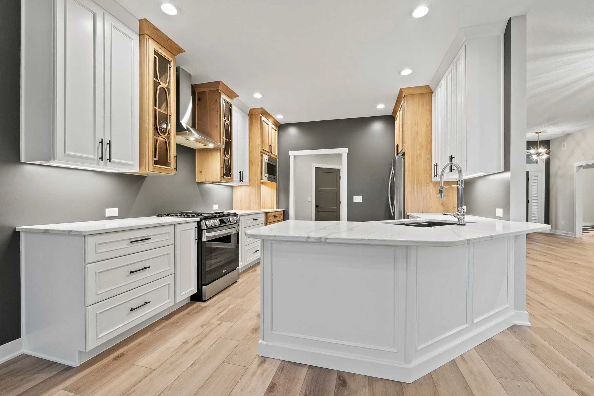 Modern kitchen with white cabinetry, marble countertop island, stainless steel appliances, gray and wooden accents, and hardwood floors.