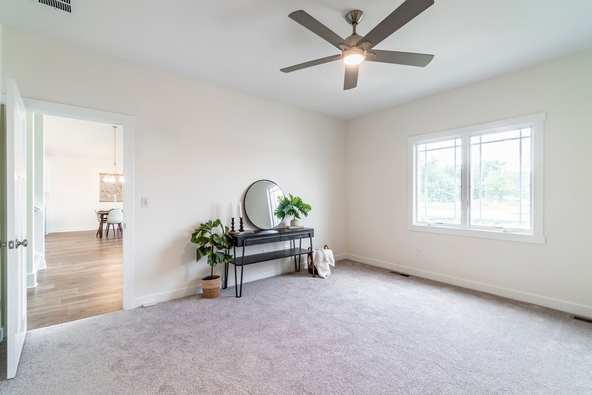 Empty living room with a ceiling fan, large window, and a black console table with a mirror, plants, and candles.