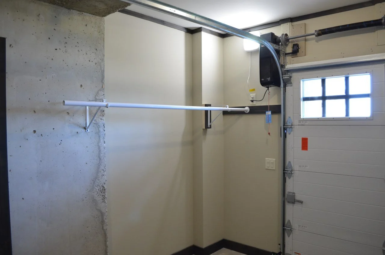 Garage with a mounted white PVC pipe, a garage door with window panes, a wall-mounted electronic device, and a small window, with concrete and painted walls.