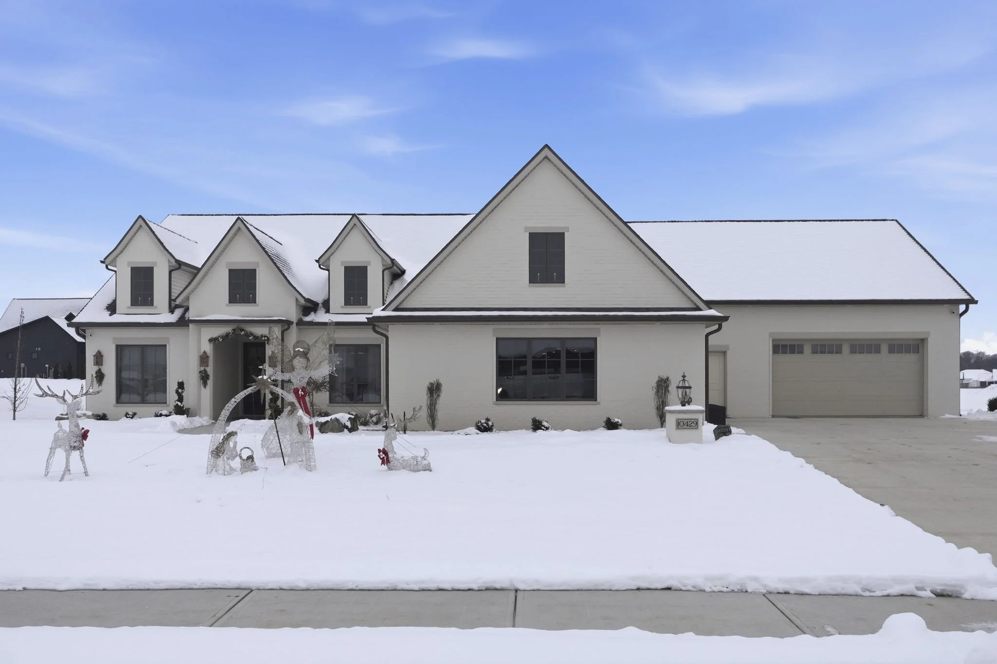 Front view of a white house with snow-covered lawn and holiday decorations, including reindeer figures and a sleigh.