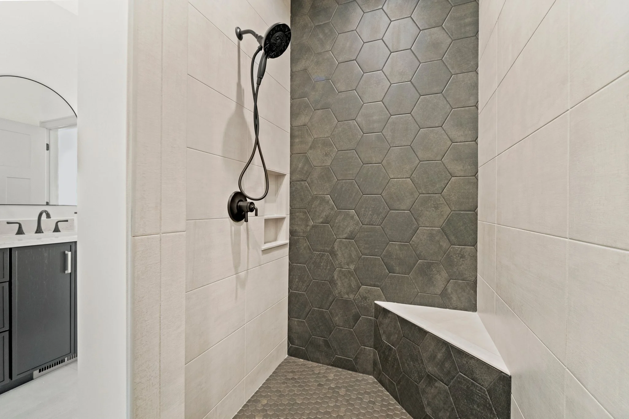 Modern shower with dark hexagonal and light rectangular tiles, built-in shelf, and a corner bench.