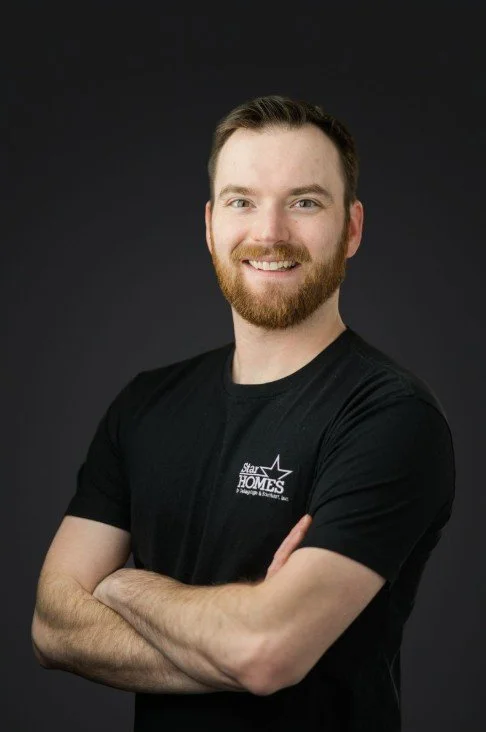 A young man with a beard and short hair smiling, wearing a black t-shirt with a logo that says 'Star Homes,' standing against a dark background.