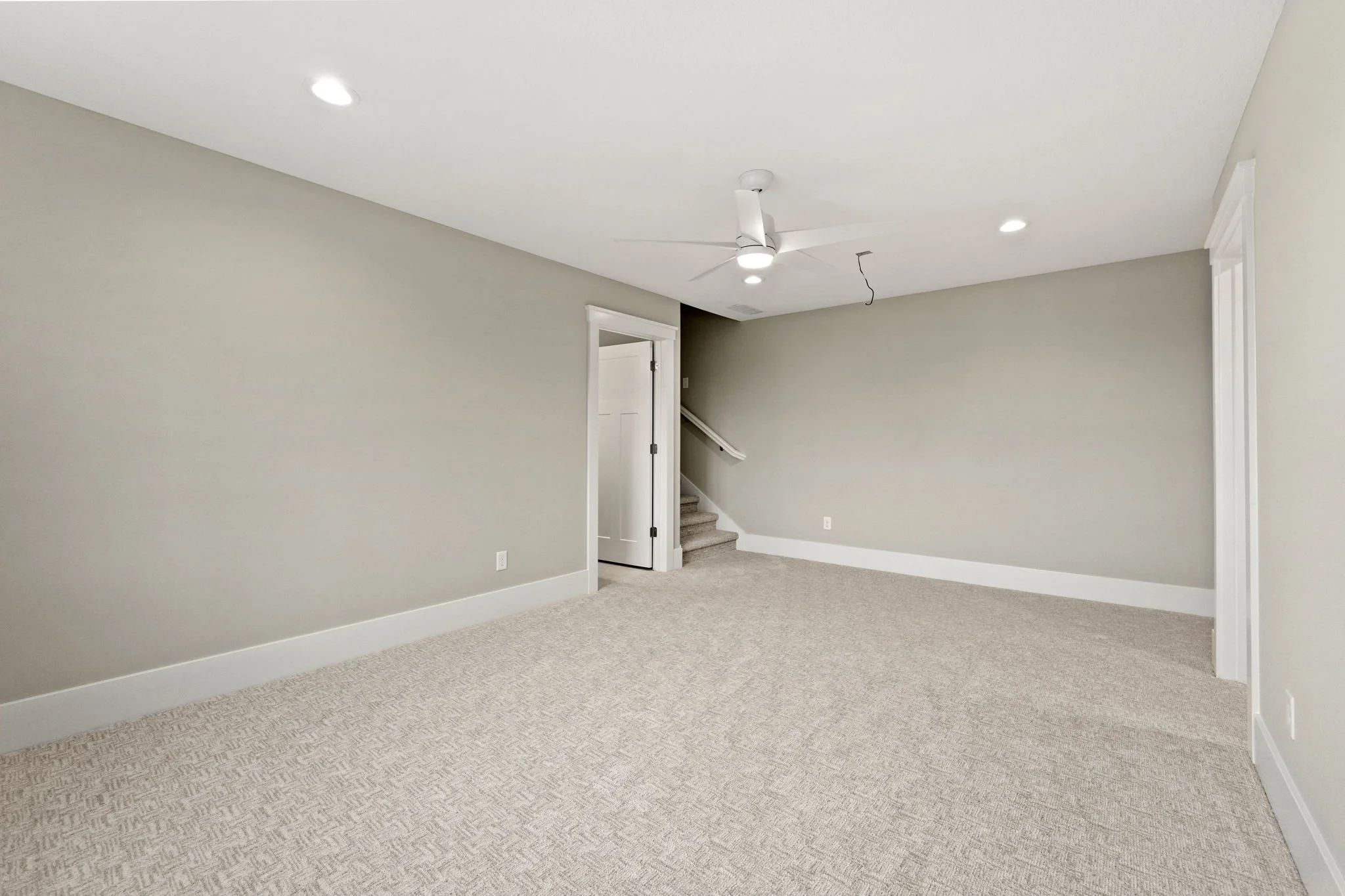 Empty room with beige carpet, light-colored walls, a ceiling fan, a small closet, and a staircase.