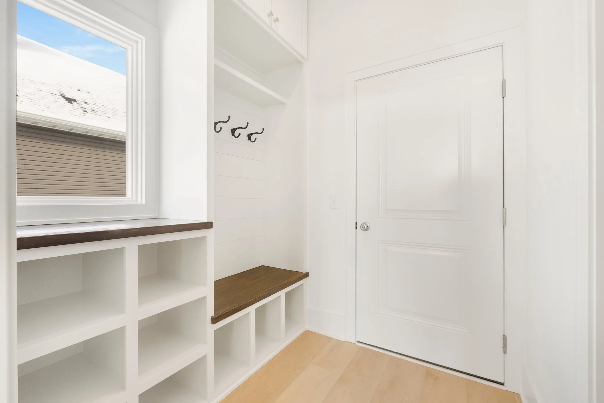 Empty entryway with built-in storage, a window, hooks on the wall, a door, and light wood flooring.