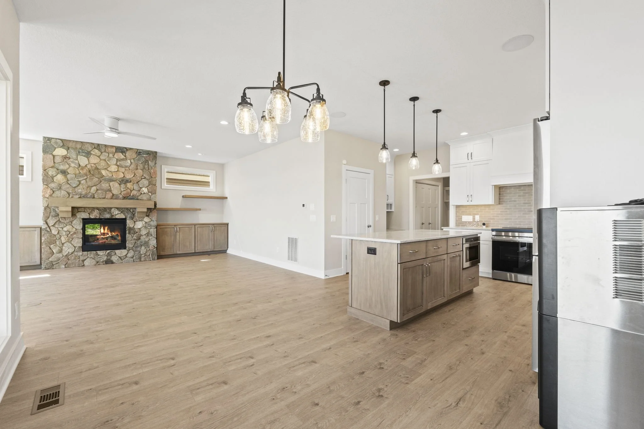 Open-concept kitchen and living room with fireplace, wooden floors, white cabinetry, and pendant lighting.