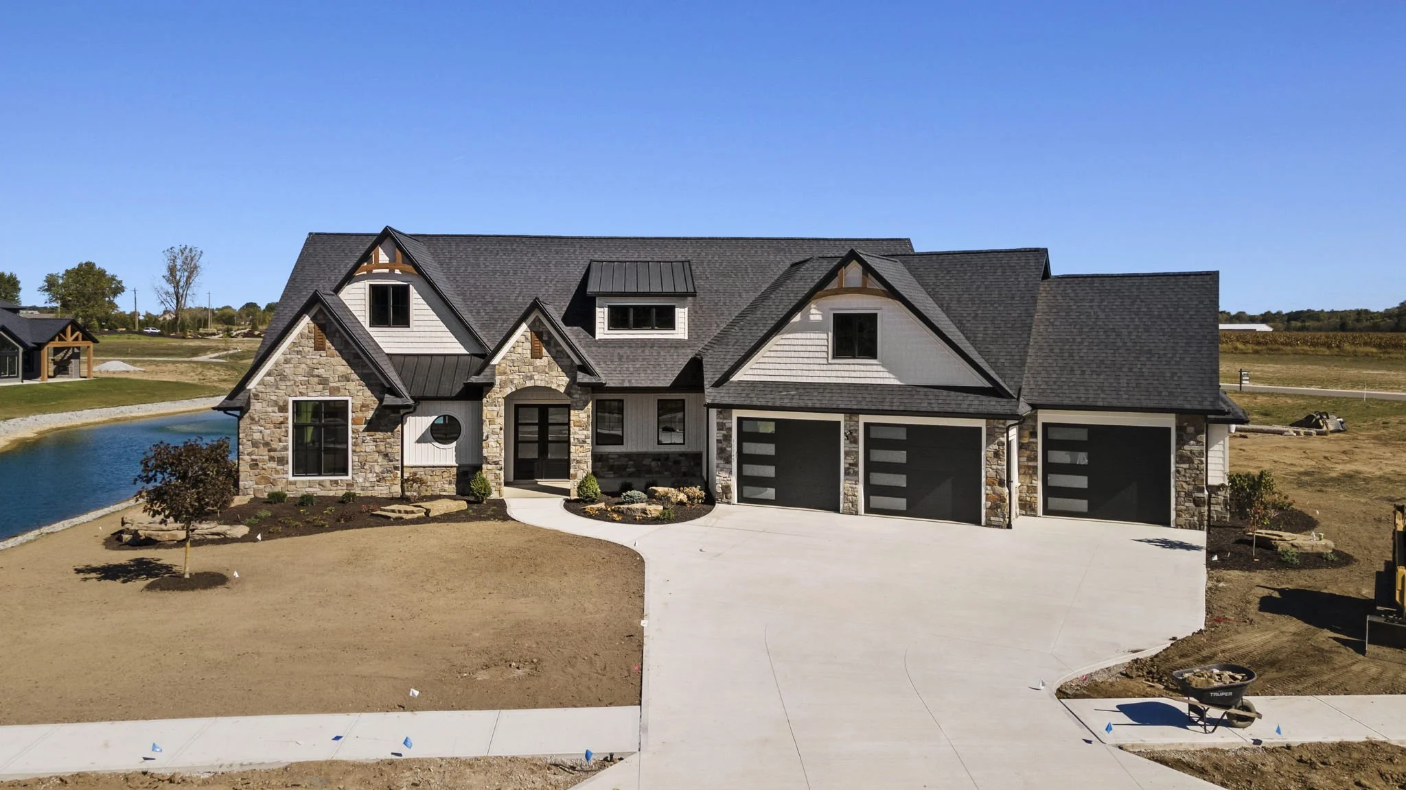 New modern house with three-car garage, stone and white siding exterior, tall roof peaks, and landscaped front yard under construction.