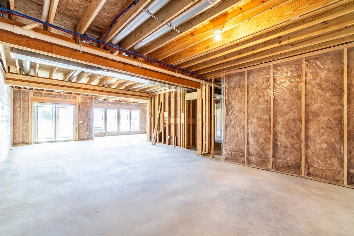 Construction site of an unfinished building with exposed wood framework, insulation on the walls, and large windows.