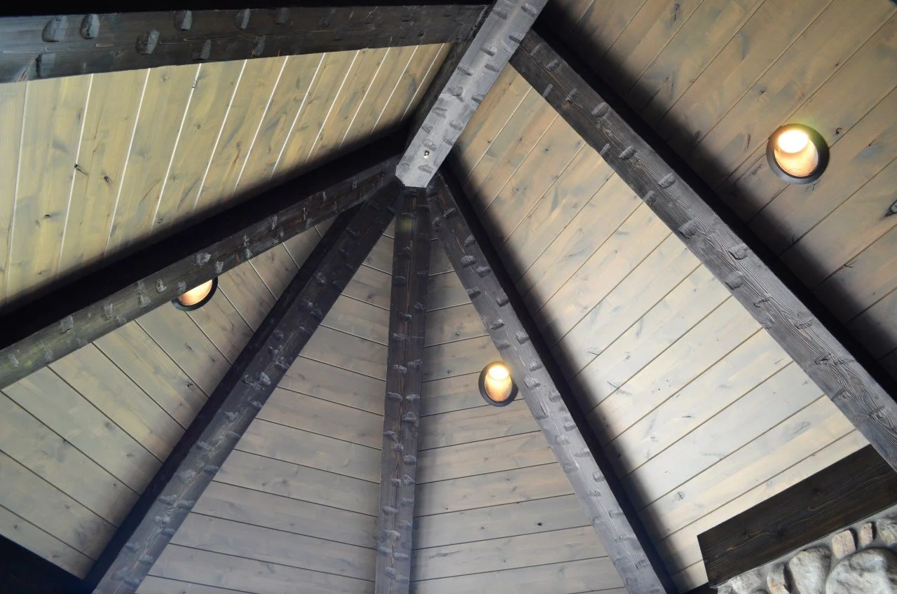 View of a wooden ceiling with beams and ceiling lights inside a structure.