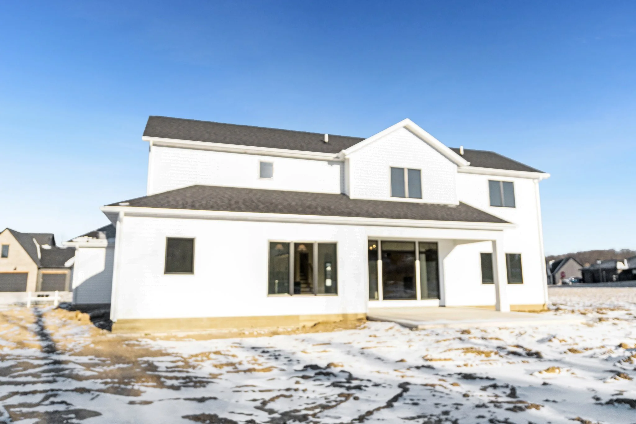 New white two-story house with black roof, large sliding door, and multiple windows, under a clear blue sky with snow on the ground.