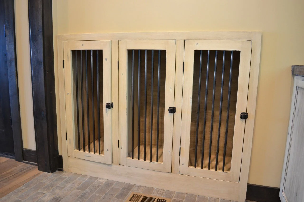 A three-door wooden pet crate with metal bars, situated against a yellow wall on a tiled floor.
