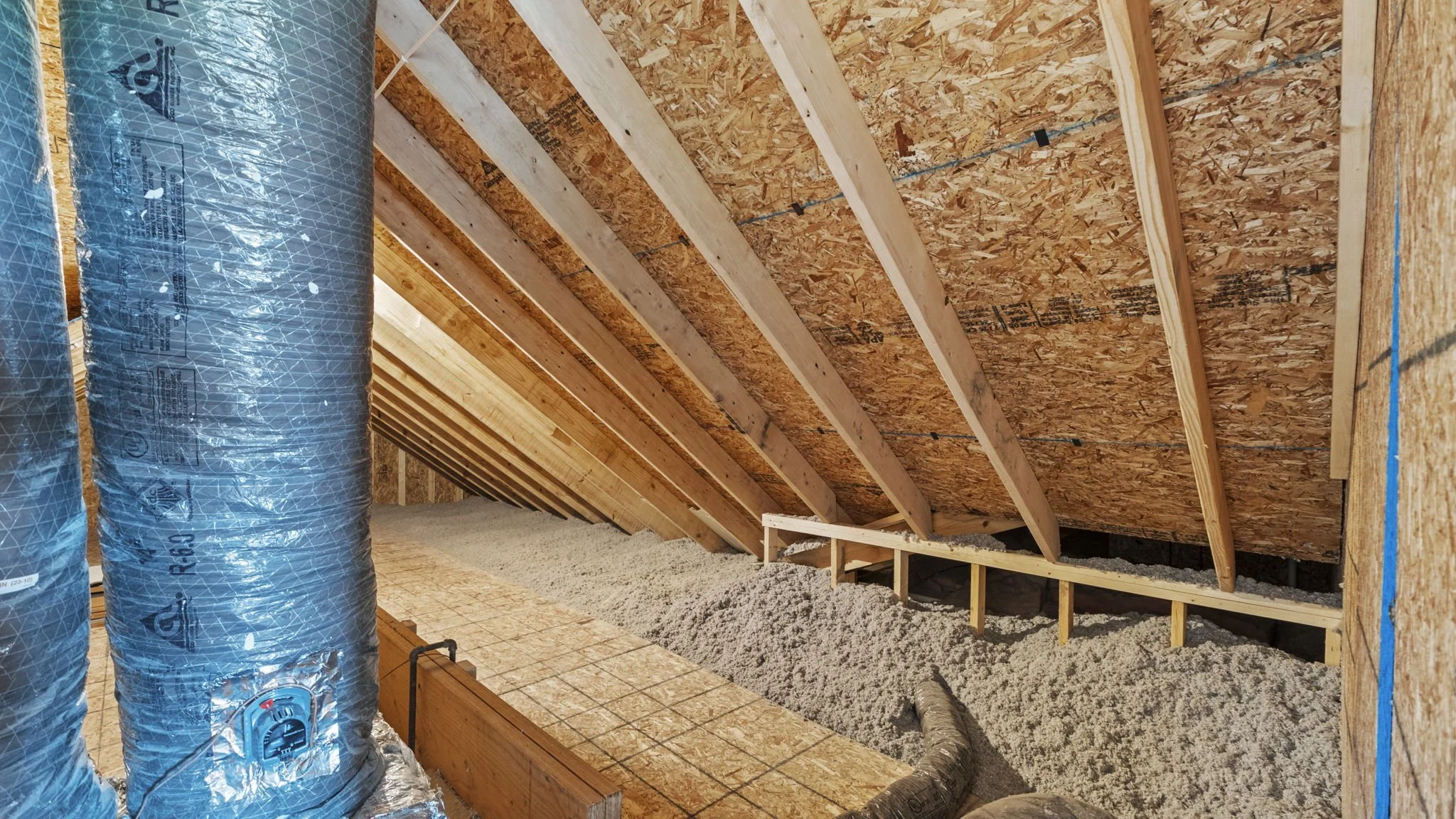 Attic space under construction with wooden beams and insulation material on the floor.