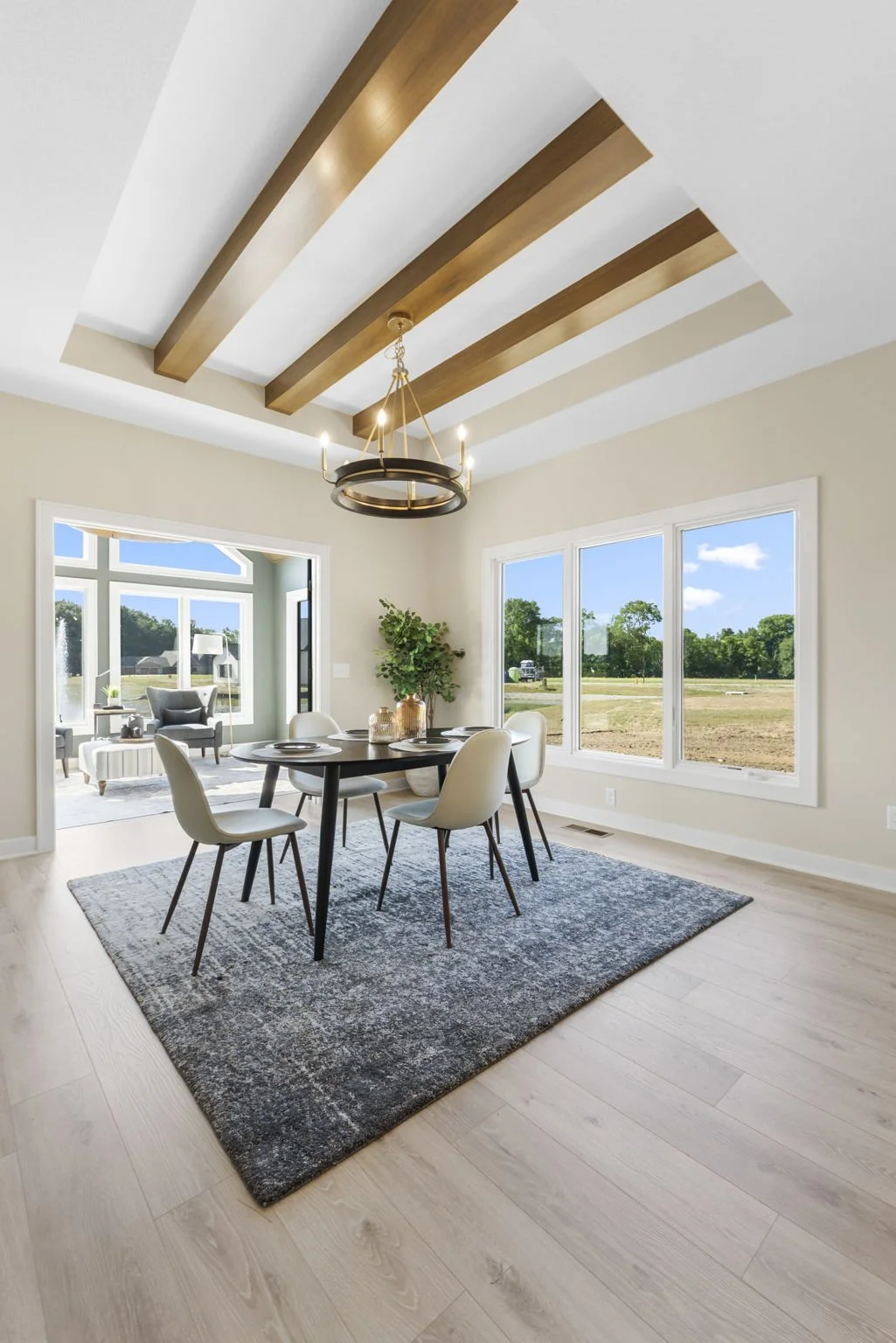 Bright dining room with black oval table, six white chairs, a chandelier, and large windows showing a green outdoor landscape.