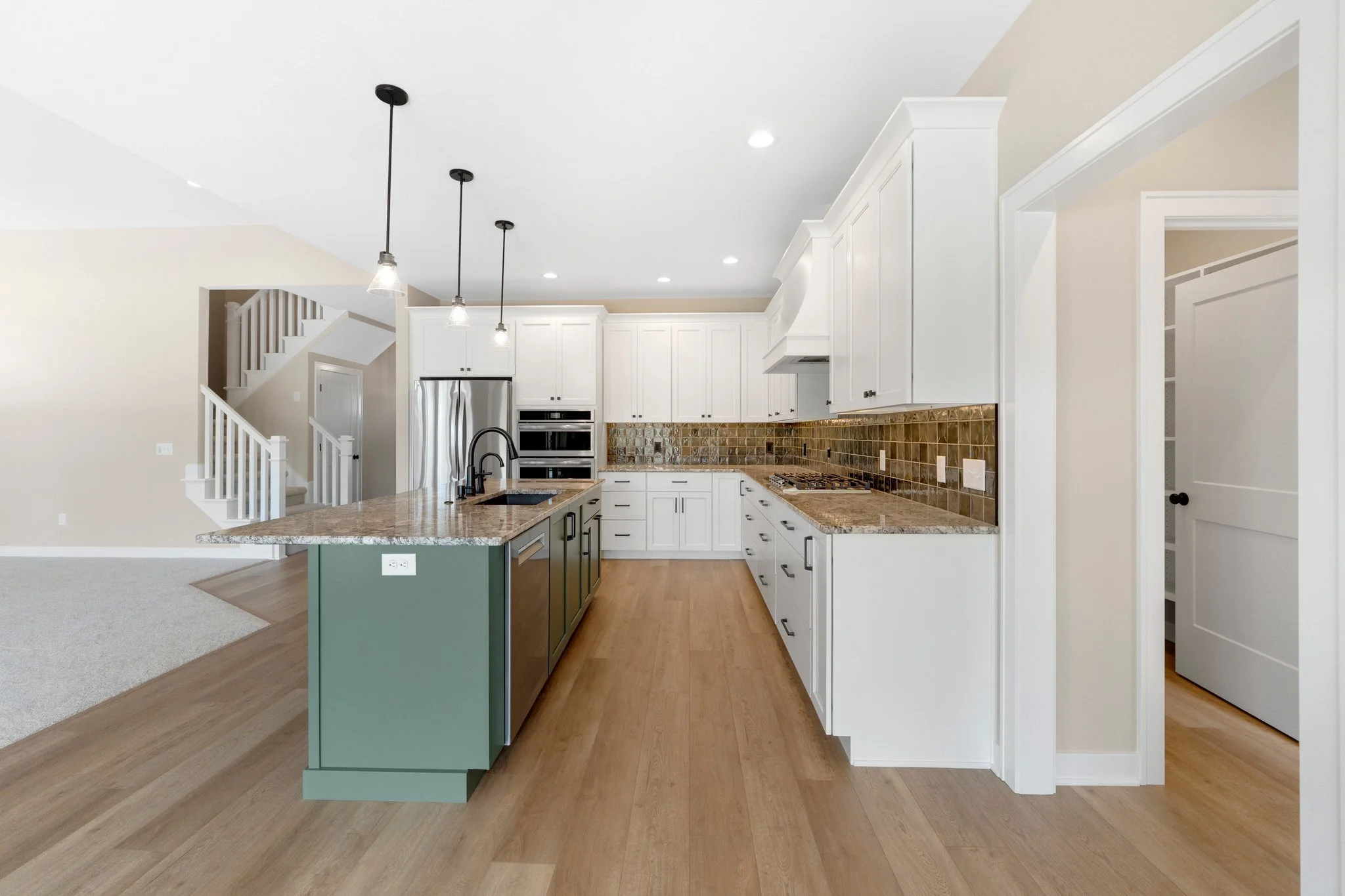 Modern kitchen with white cabinetry, brown granite countertops, a green kitchen island, and wood flooring.