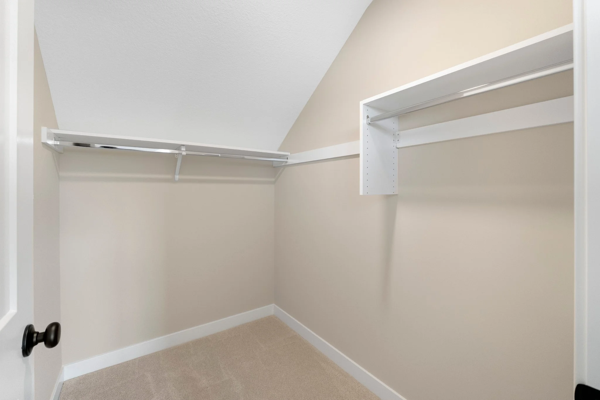 Empty walk-in closet with white shelves and beige walls.