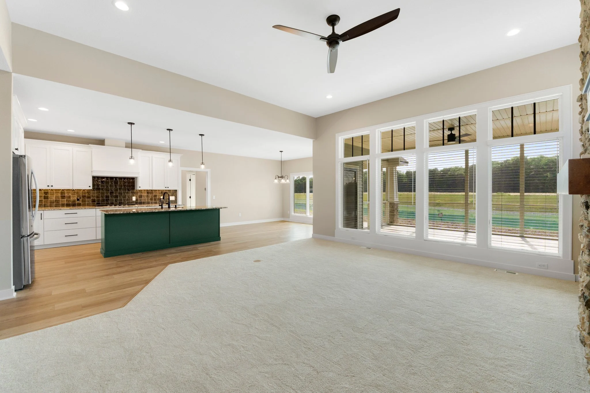 Open-concept living area and kitchen with large windows, ceiling fan, and view of backyard.