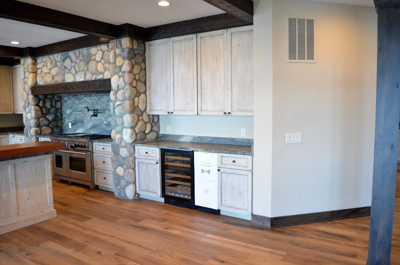 Kitchen with stone and wood accents, including a stone wall around the stove, wood cabinets, and a wine cooler.