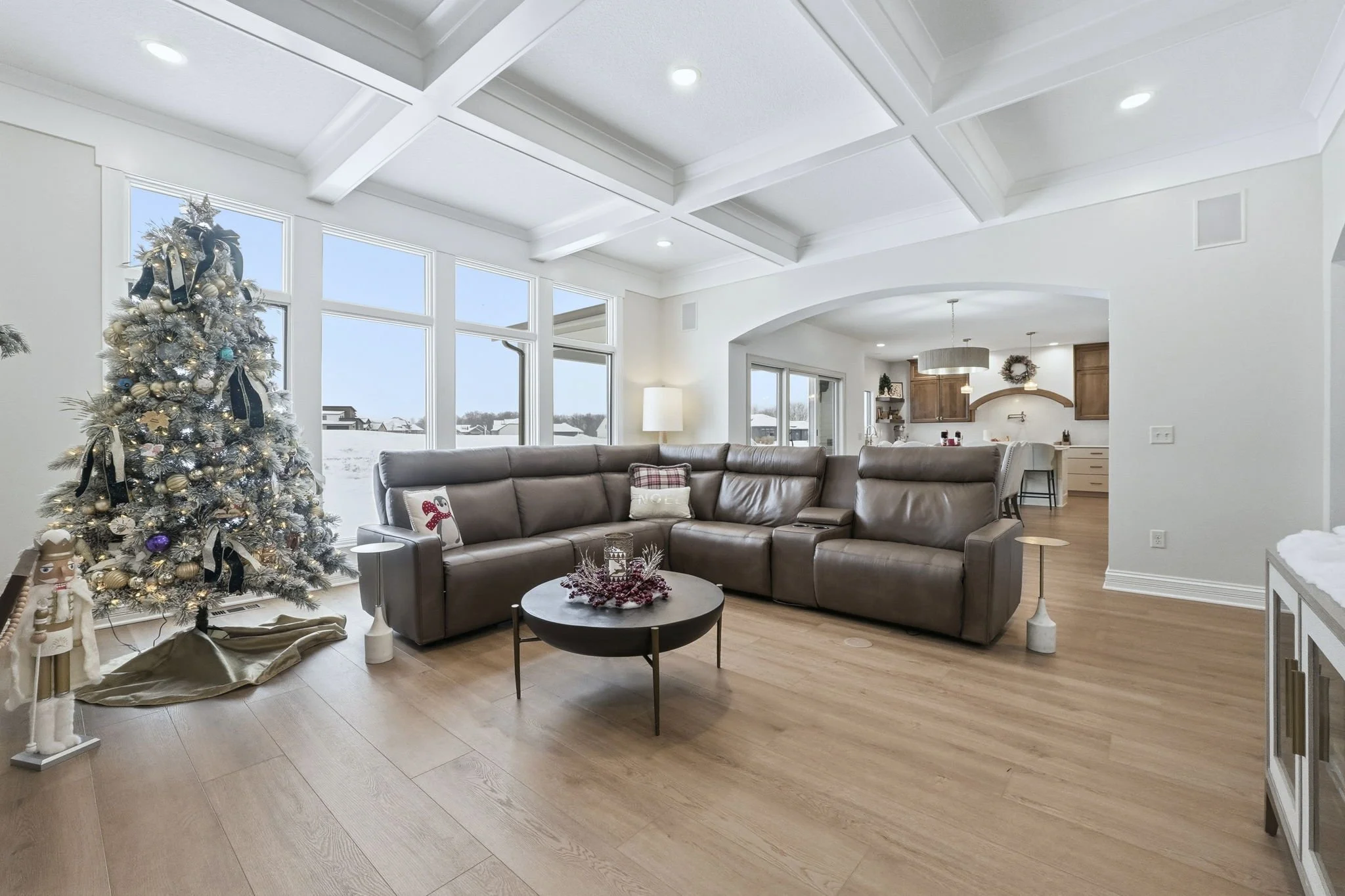 Living room with Christmas tree, sectional sofa, and holiday decorations with a view to the kitchen, decorated for Christmas.