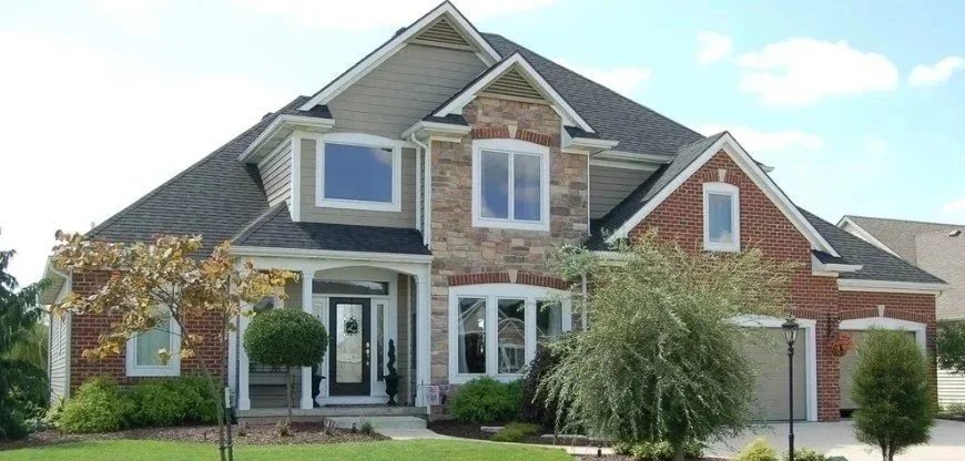 A two-story suburban house with a brick and stone facade, front porch, well-maintained landscaping, and a garage on the right side.