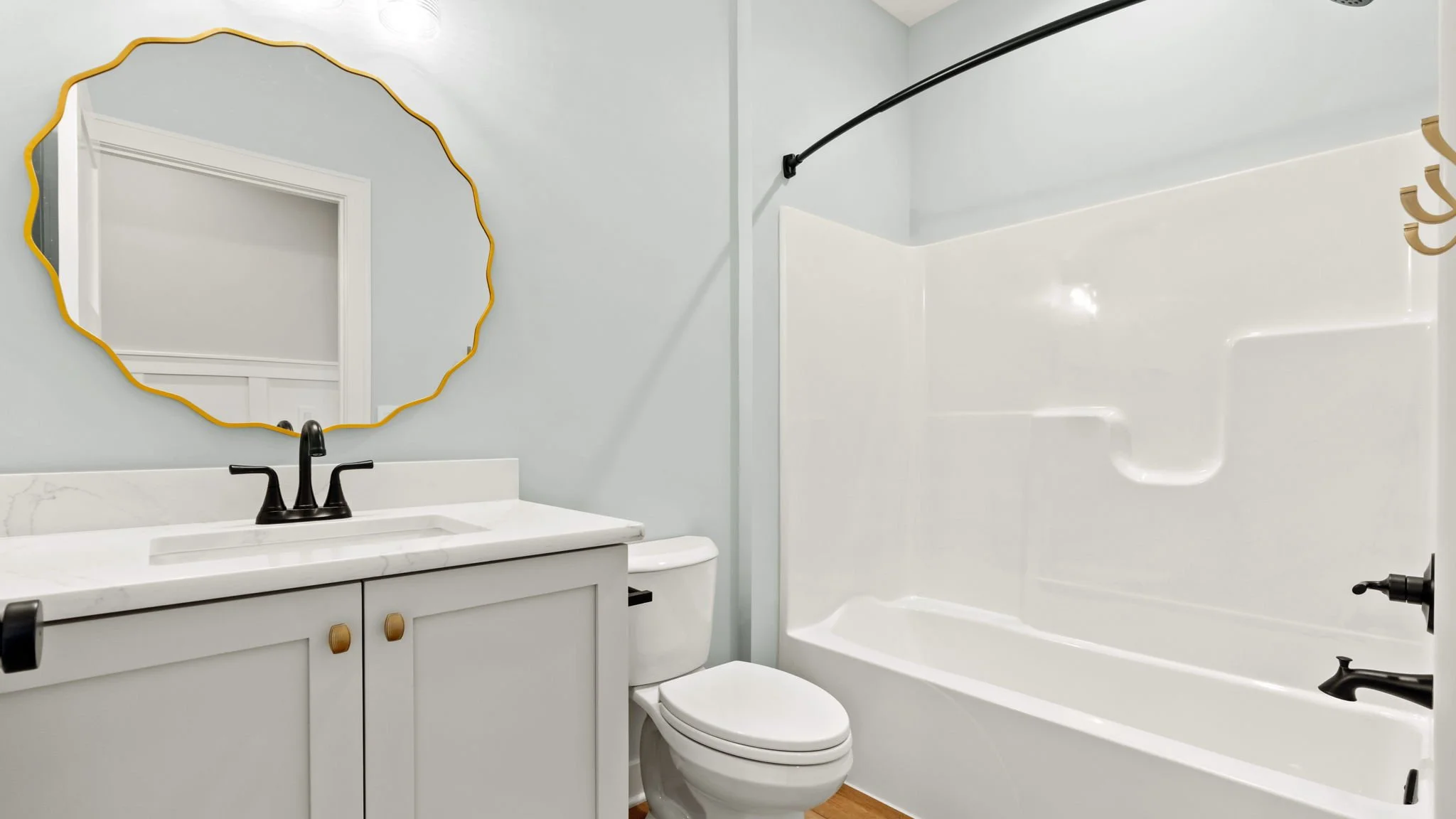 Bathroom with white vanity, marble countertop, black faucet, round mirror with yellow frame, white toilet, and bathtub with black fixtures.