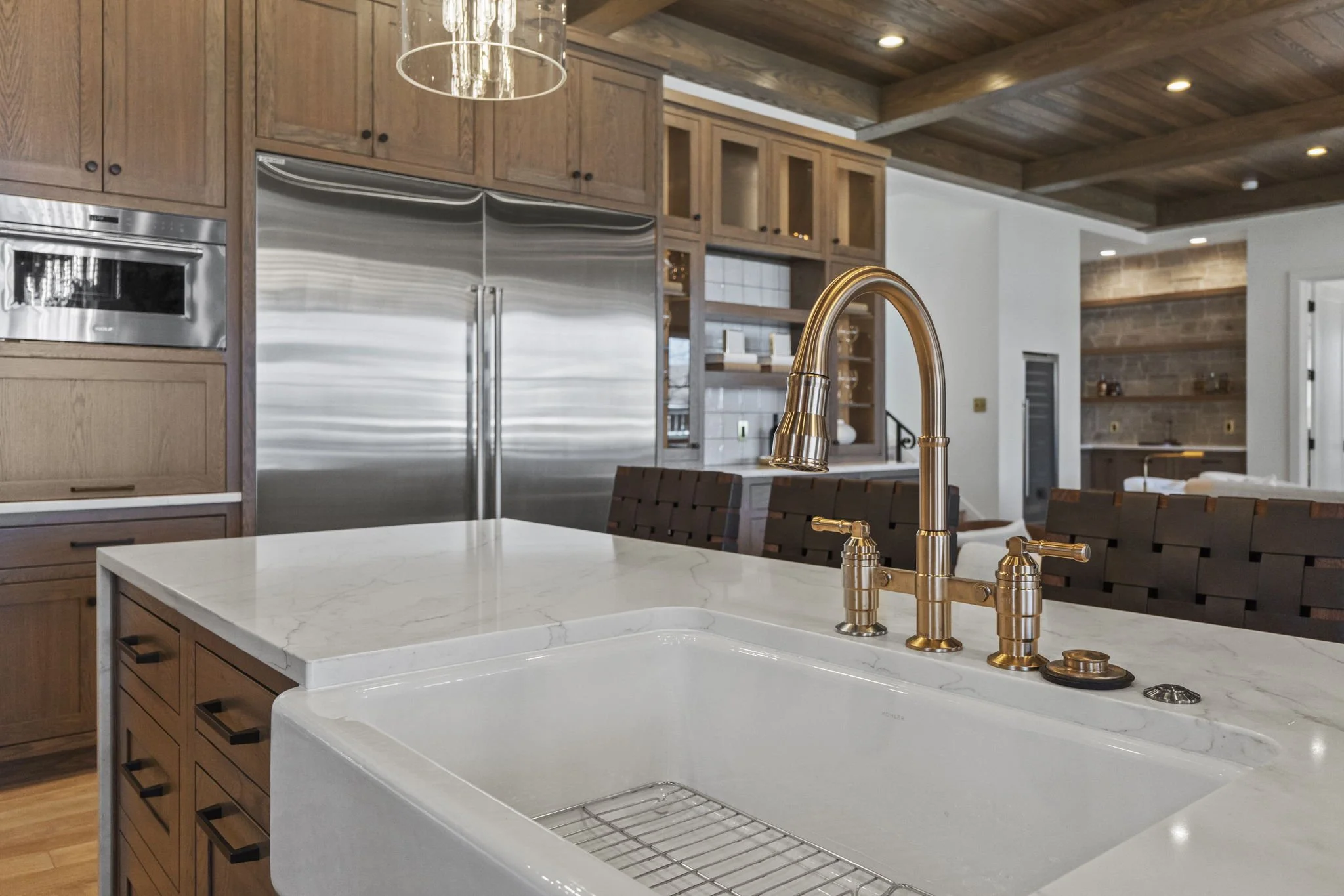 Modern kitchen with white marble countertop, large stainless steel refrigerator, wooden cabinets, and a gold sink faucet.