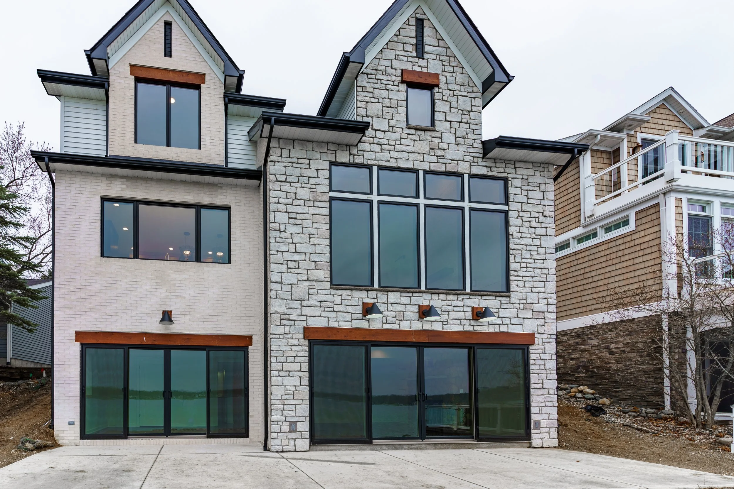 Modern multi-story house with large windows, a stone facade, and a concrete driveway.