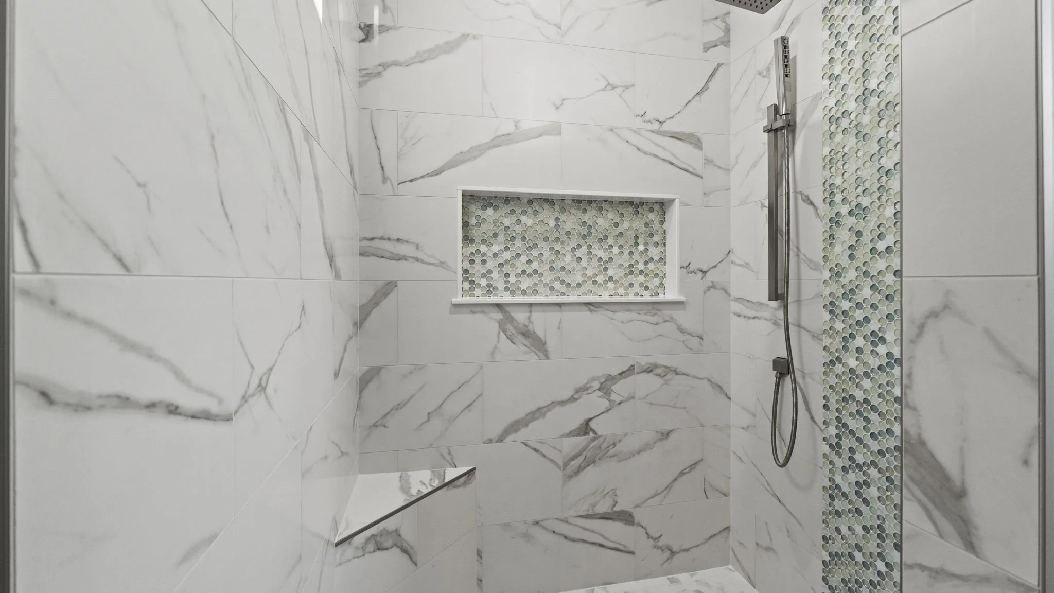Modern bathroom shower with white marble tiles, a built-in shelf with mosaic tiles, and a showerhead with a hose.
