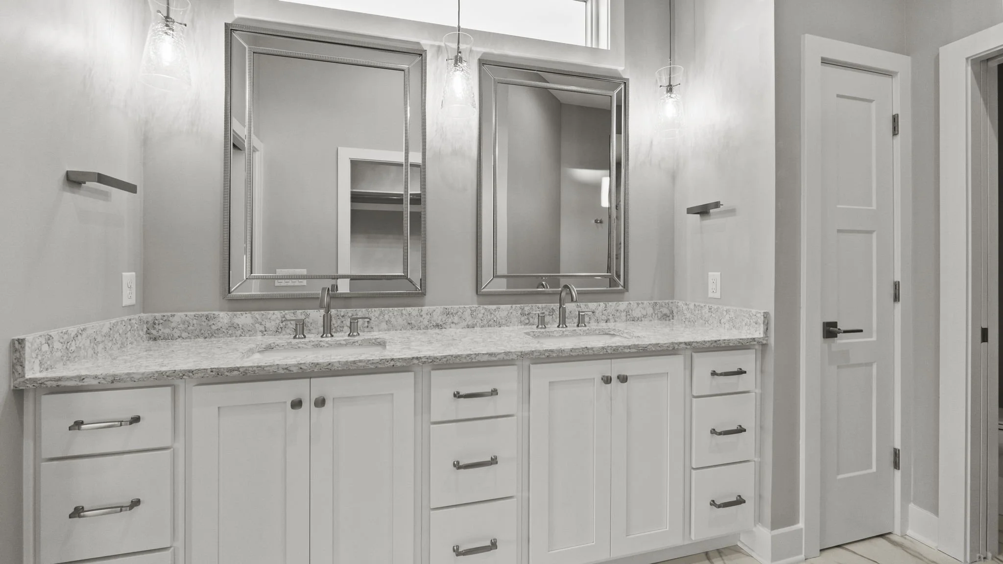 Modern bathroom vanity with two white sinks, granite countertop, two large mirrors, three light fixtures, and white cabinetry with silver handles.