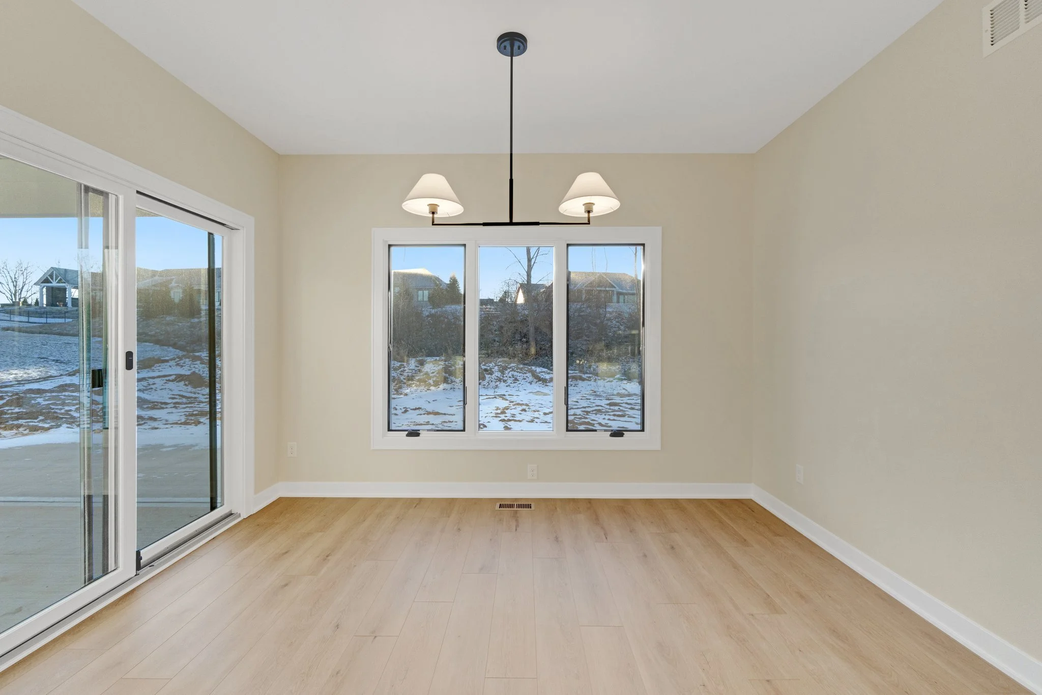 Empty room with light wood flooring, beige walls, white trim, a large window, and sliding glass door, with snow outside.