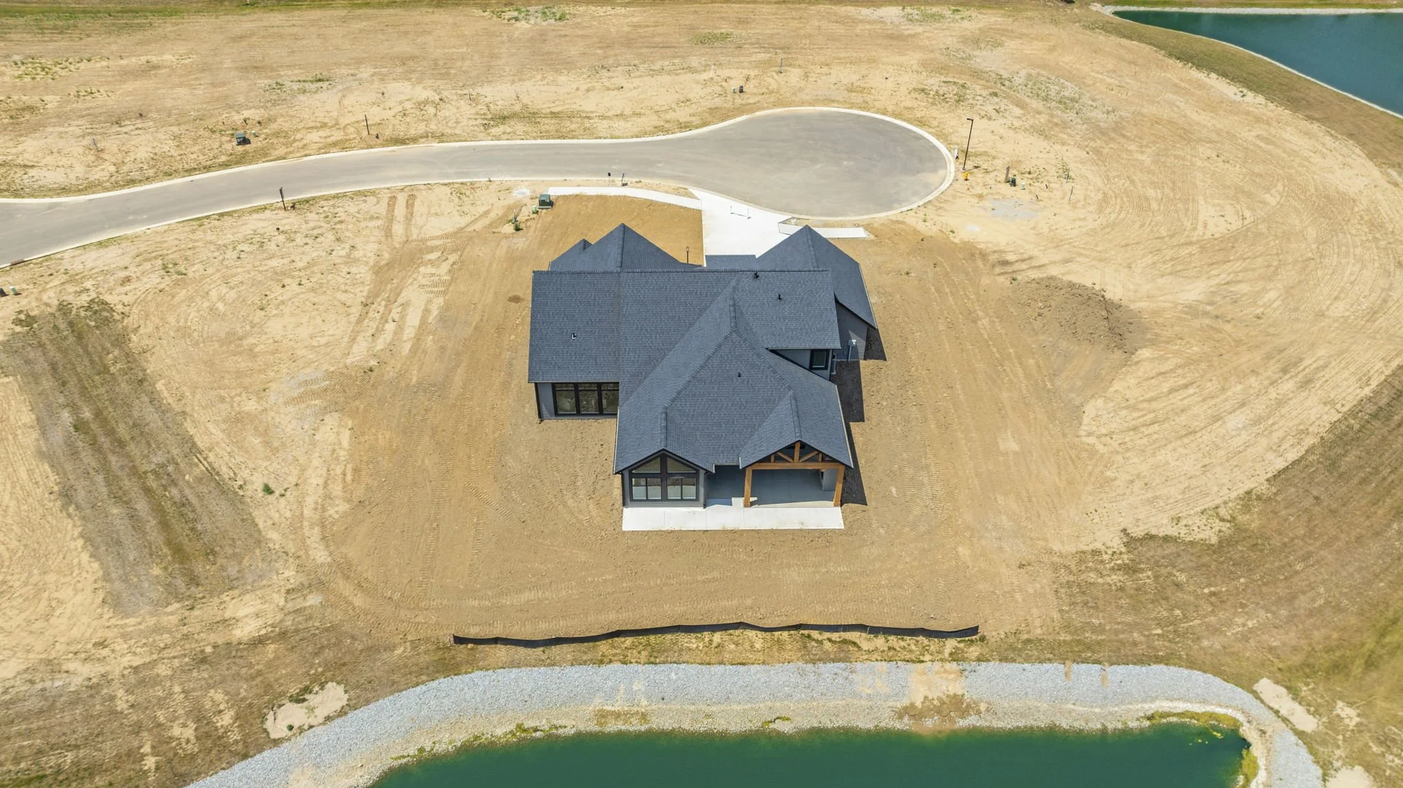 Aerial view of a newly constructed house on a cleared lot next to a body of water.