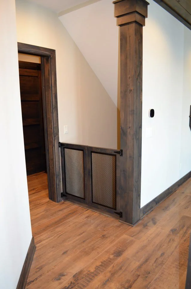 Wooden interior with a small gate on the staircase, featuring two mesh panels, and wooden trim around the doorframe and baseboards.