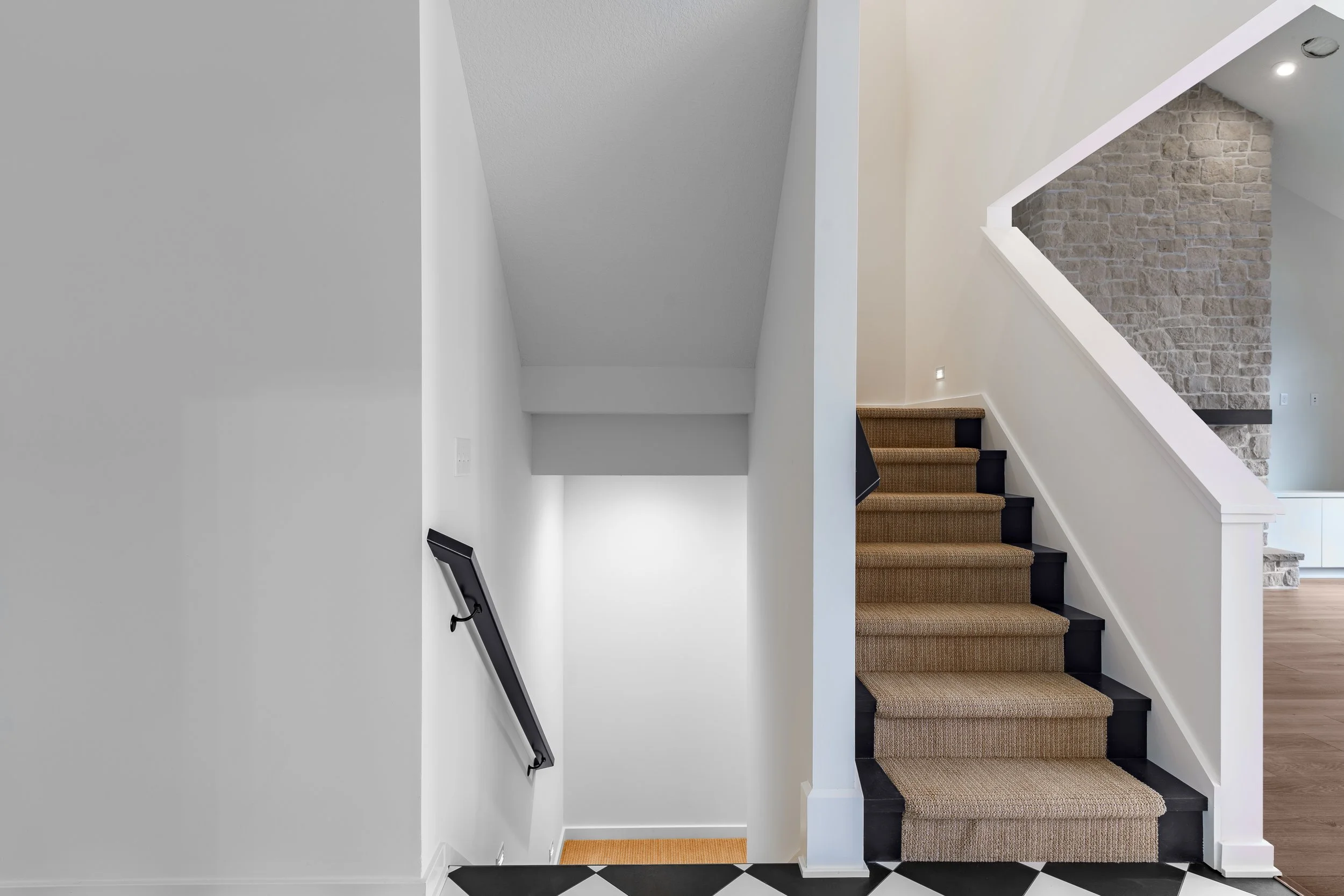 Interior view of a staircase with beige carpet runners and white railings against a partial brick wall in a modern home.
