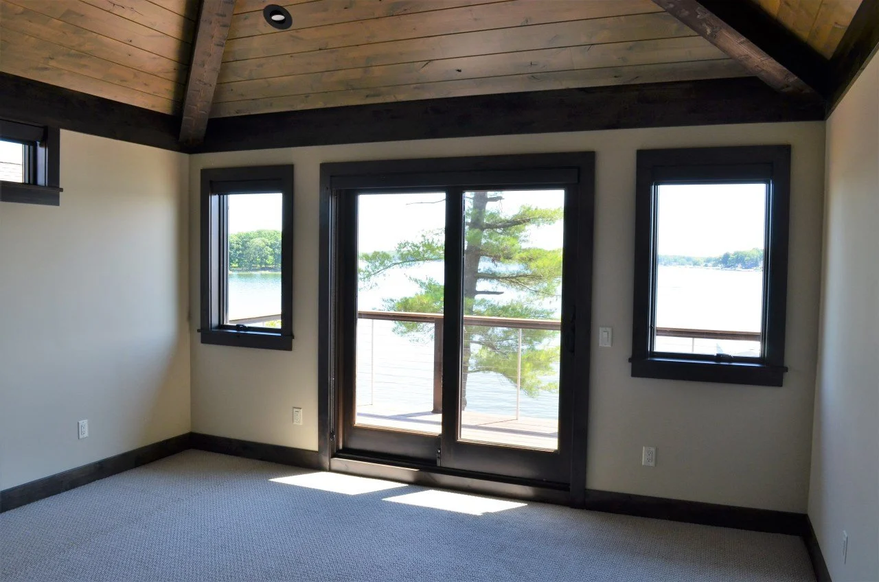 Interior of a room with large windows and a sliding glass door overlooking a lake and trees outside.