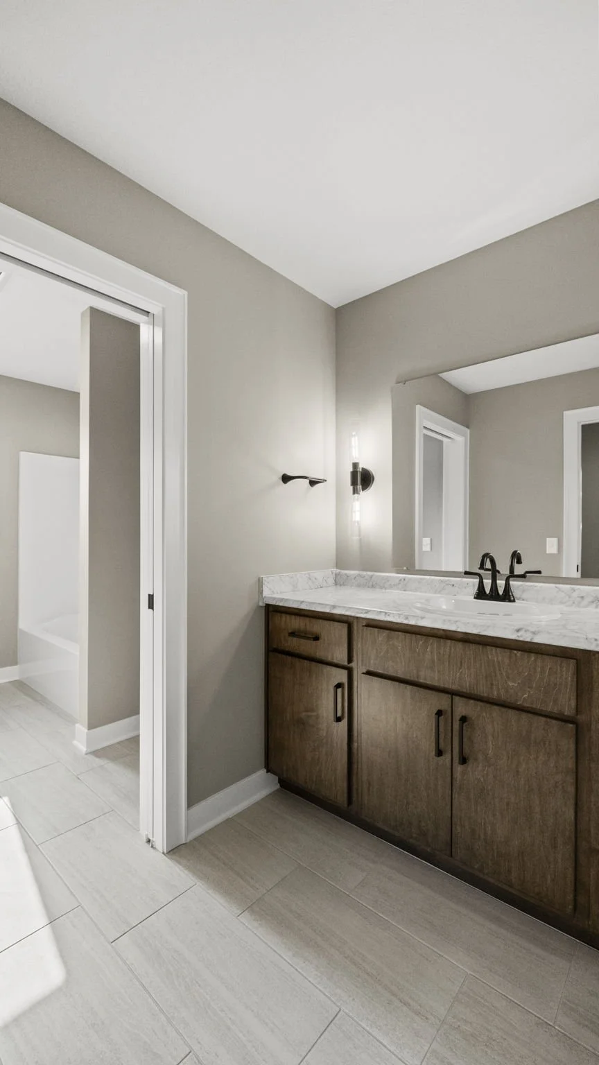 Modern bathroom with a wooden vanity, marble countertop, double black faucet, wall-mounted light fixtures, and a mirror, with light-colored tiled flooring and neutral walls.