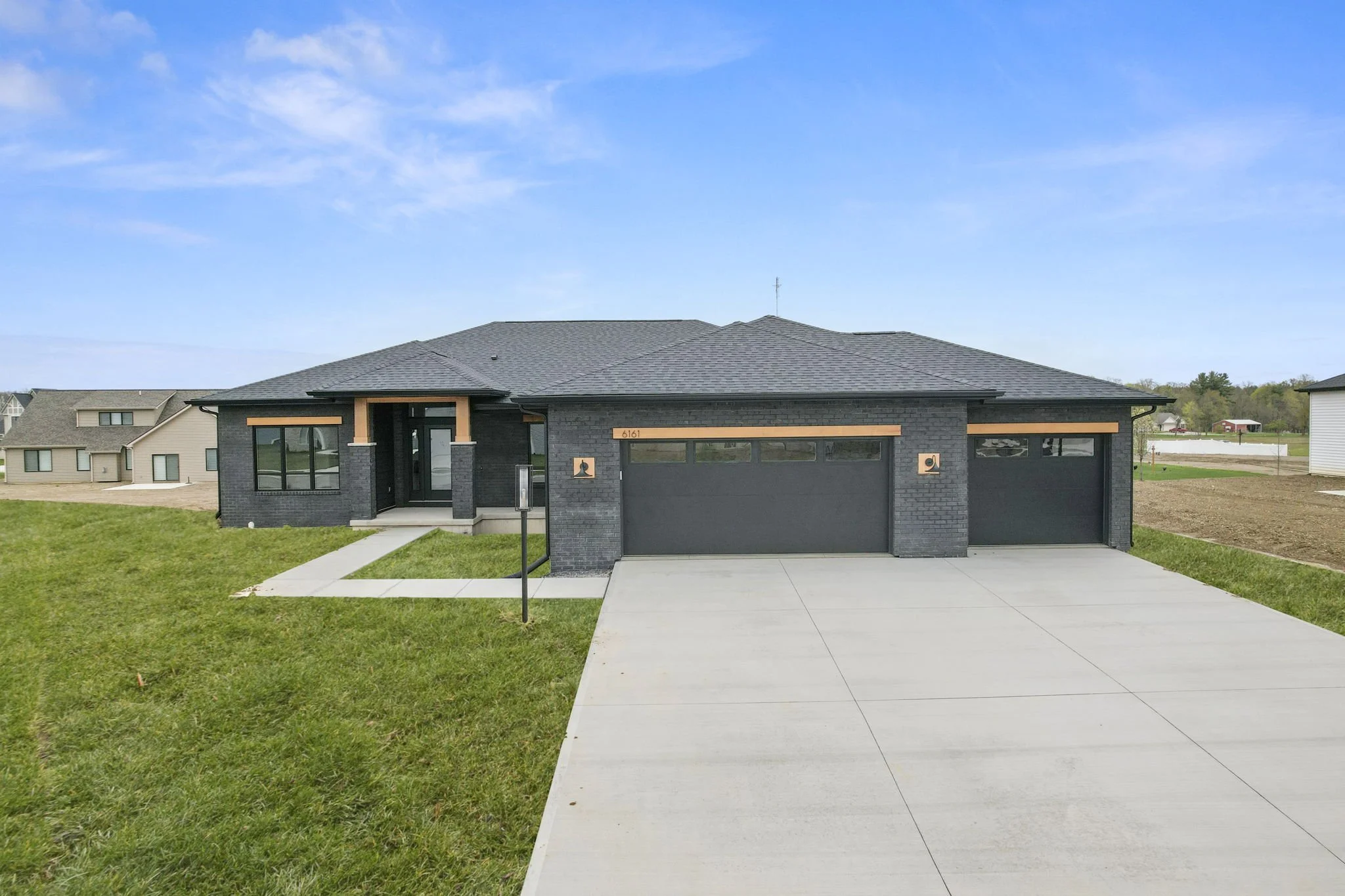 New modern house with black exterior, two car garage, front lawn, and concrete driveway under a blue sky.