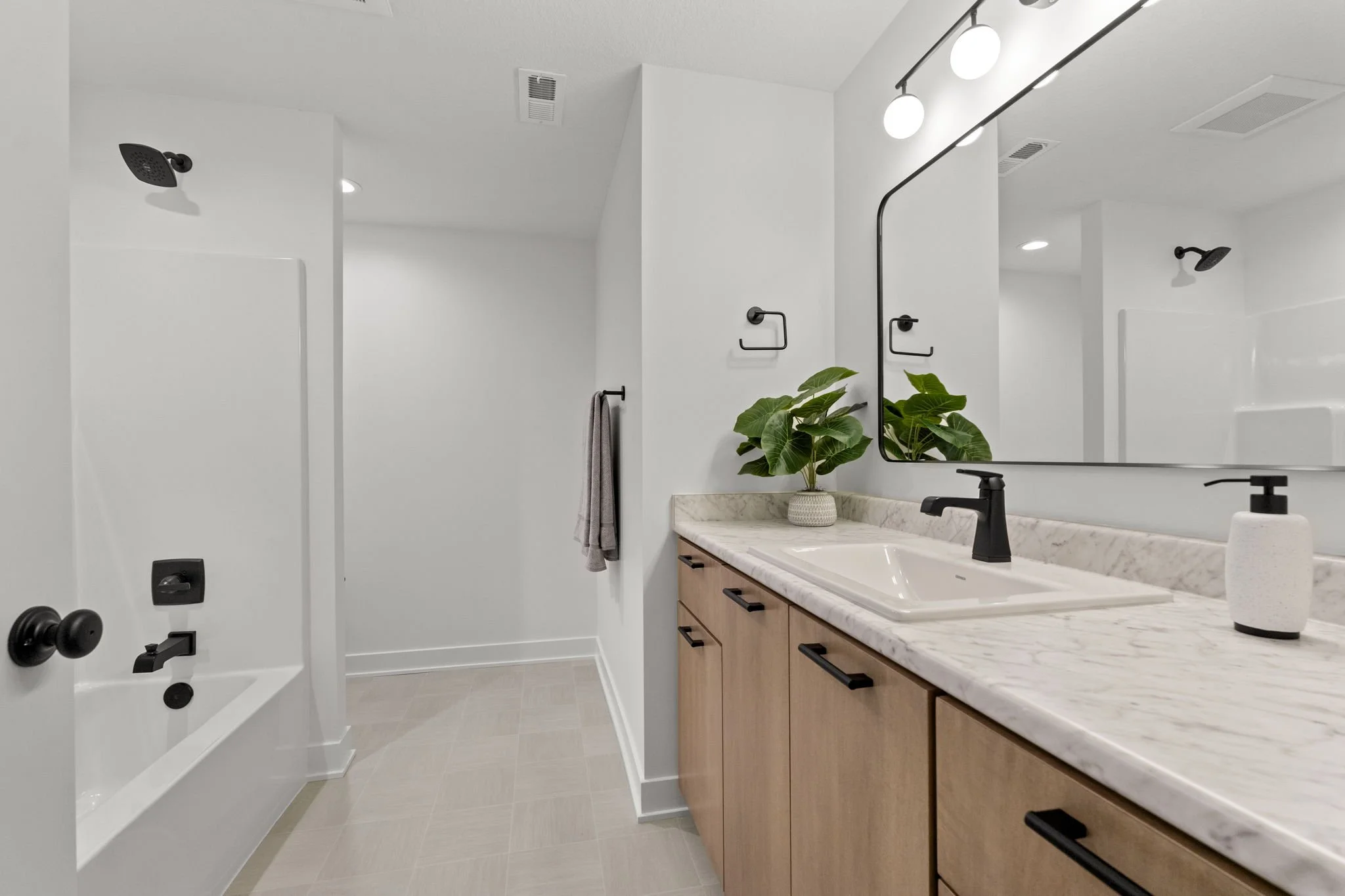 Modern bathroom with a marble countertop, black fixtures, a large mirror, a plant, and a towel on a rack.
