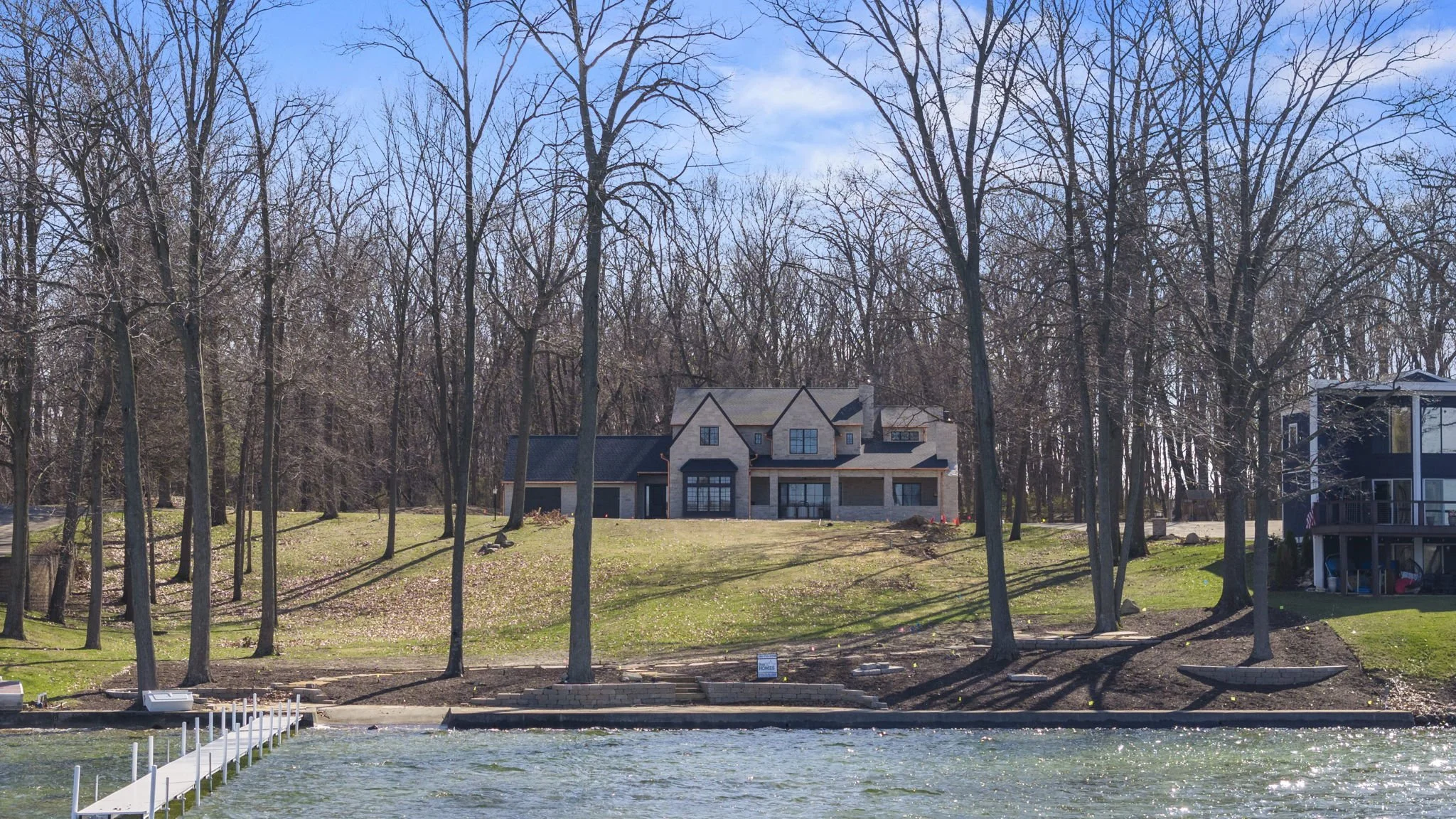 A house on a hill by a river with trees and a dock in the foreground.