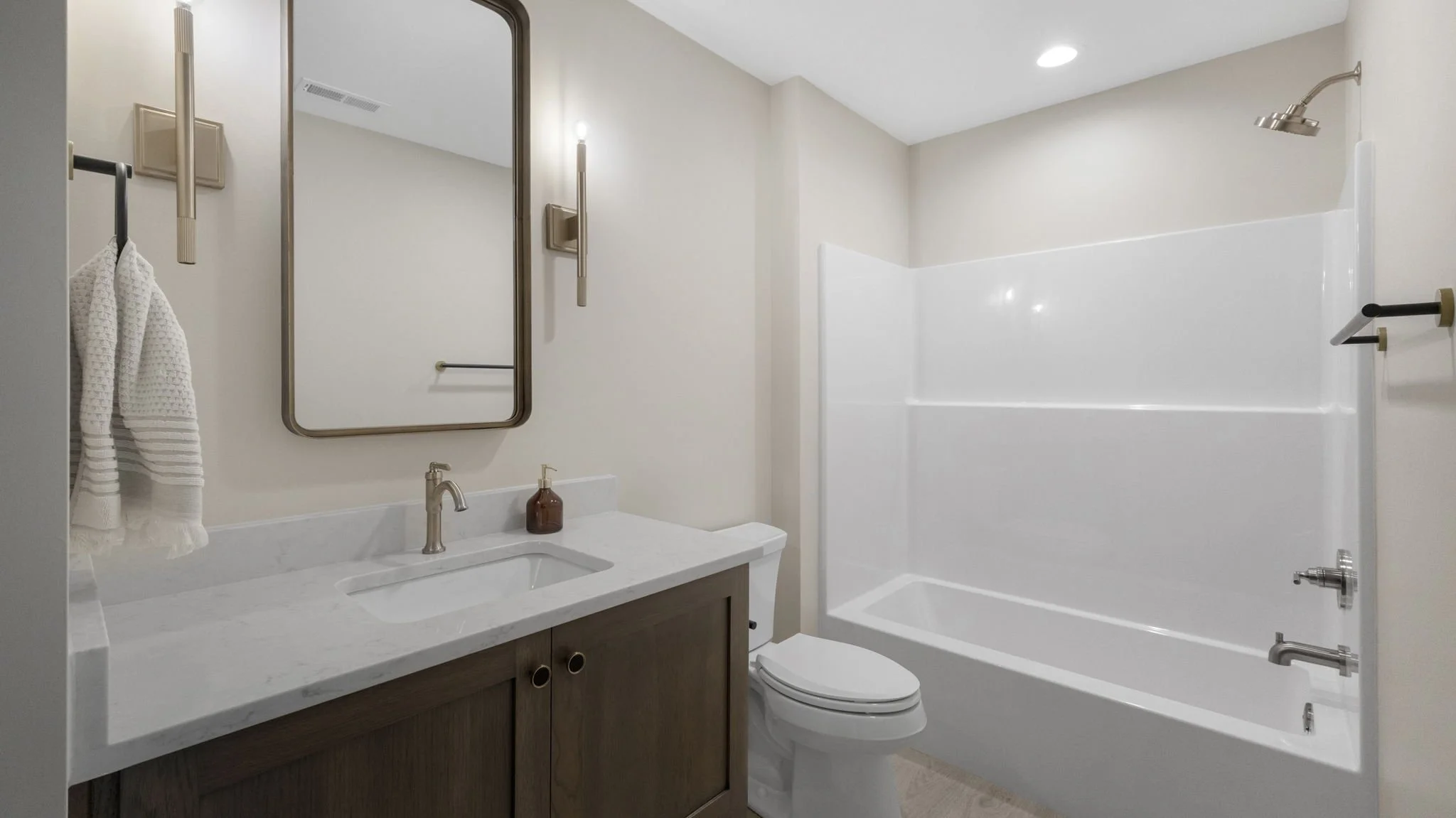 A modern bathroom with a white bathtub, a toilet, and a vanity with a sink, mirror, and wall-mounted lights.