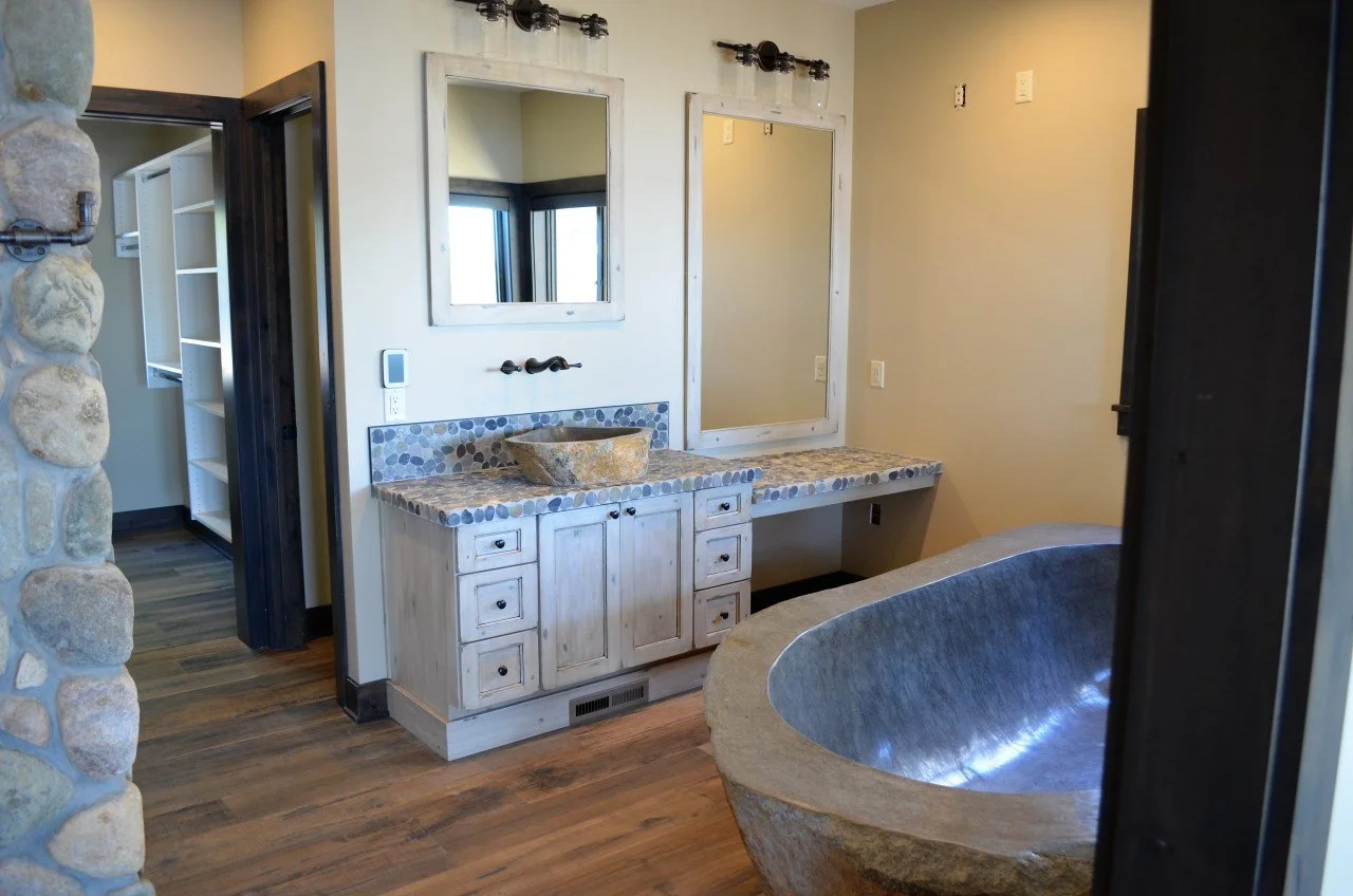 Bathroom with stone bathtub, wooden vanity with stone sink, and large mirrors above the vanity.