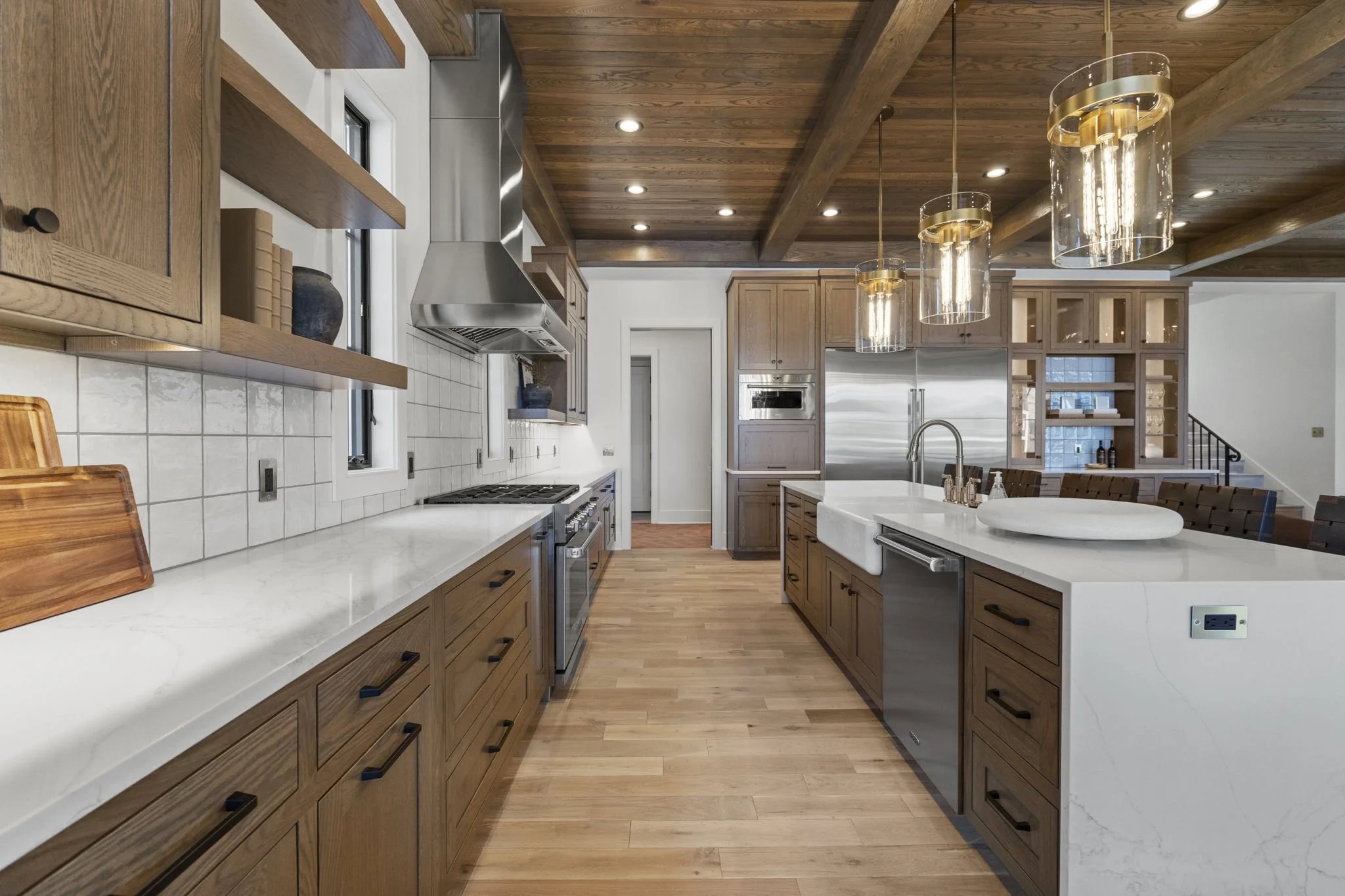 Modern kitchen with wooden cabinets, white island with sink, stainless steel appliances, pendant lights, and hardwood floors.