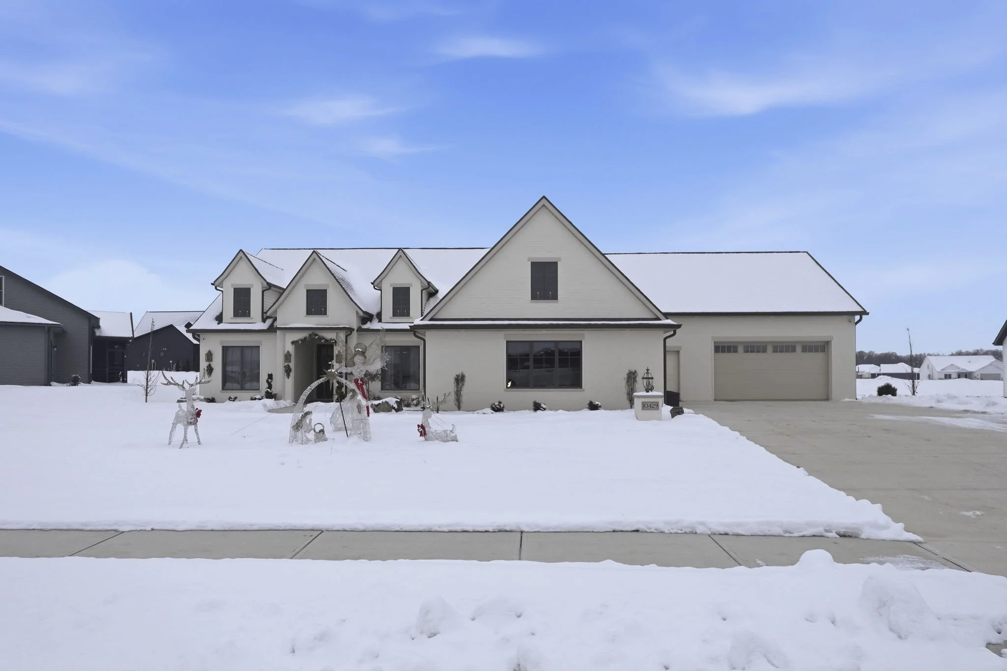 A white house with a snow-covered front yard and decorative holiday lights, during winter with a partly cloudy sky.