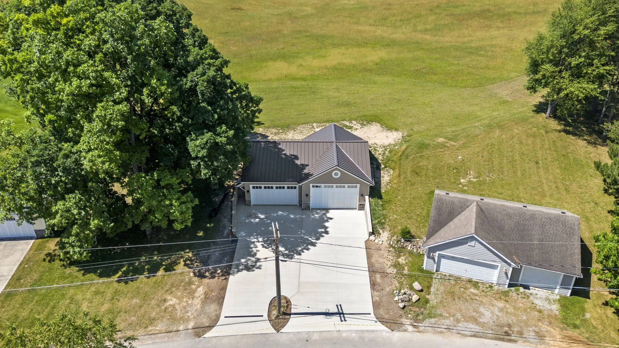 Aerial view of two detached garages with driveways, surrounded by trees and grassy areas, in a suburban neighborhood.