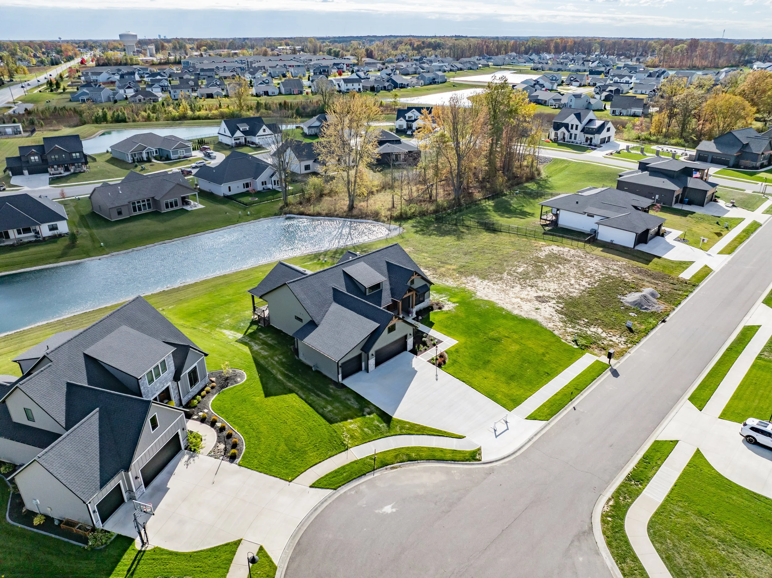 Aerial view of a suburban neighborhood with houses, manicured lawns, a pond, and trees.
